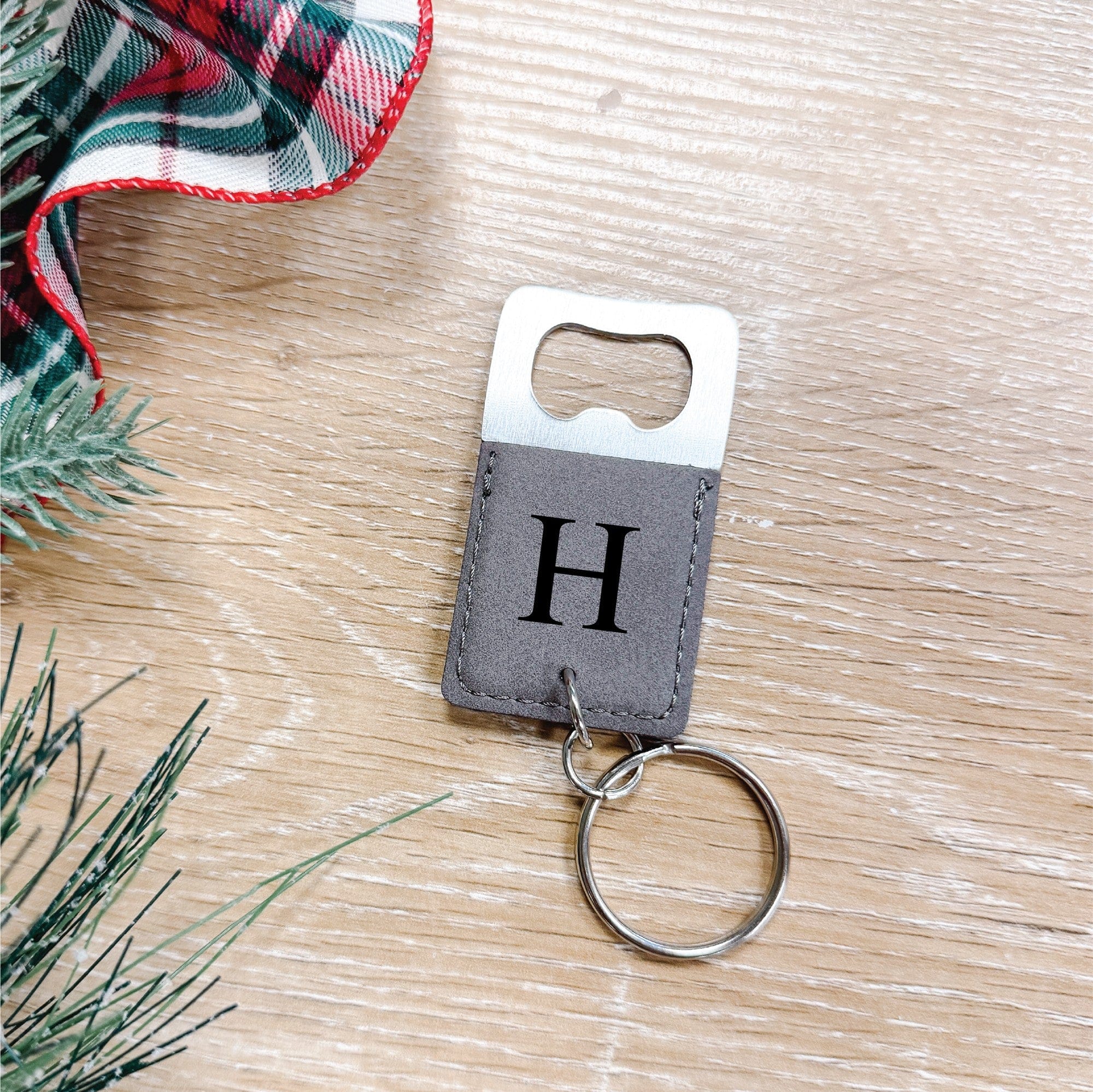 A personalized bottle opener keychain featuring a gray faux leather sleeve with a stitched edge, a silver metal opener, and an attached key ring.