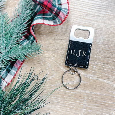 A personalized bottle opener keychain featuring a silver-toned metal opener and a textured black leatherette handle with white stitching, suitable for wedding favors or holiday event gifts.