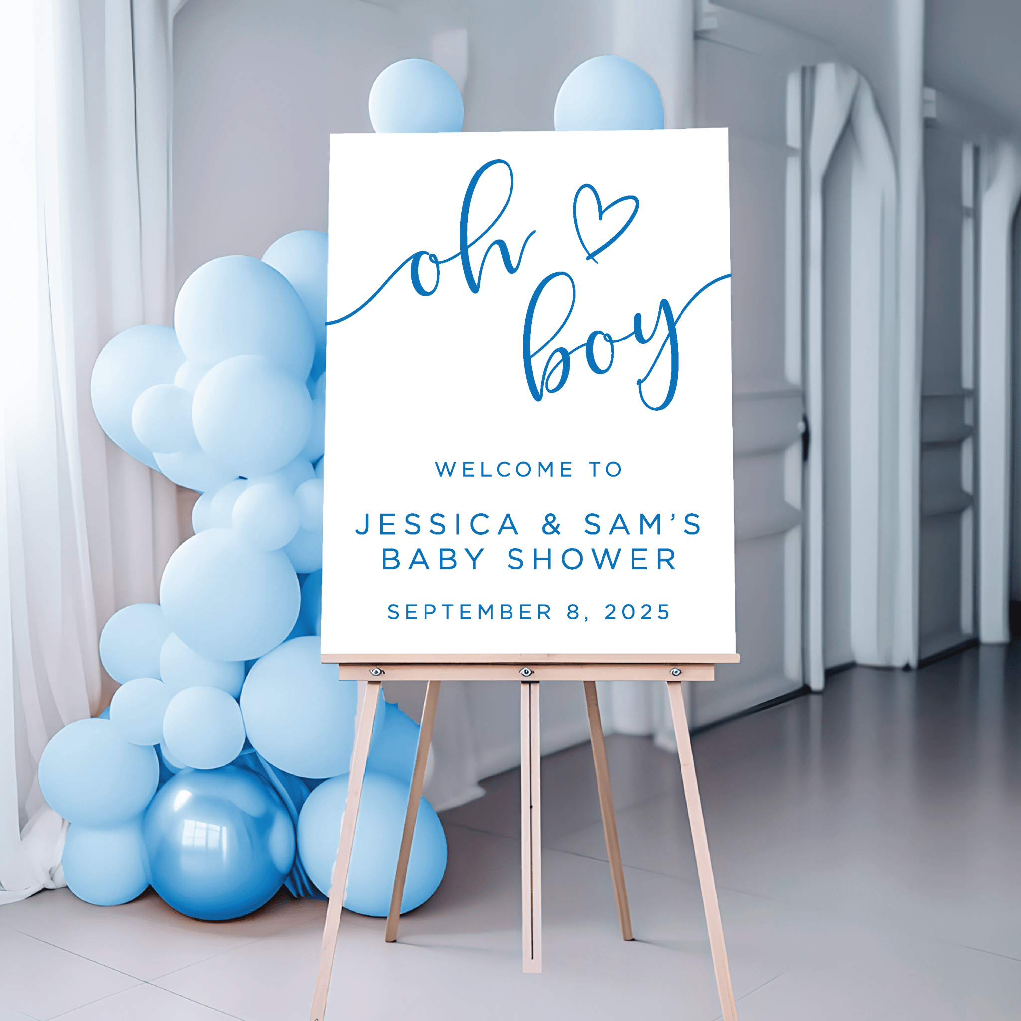 White acrylic welcome sign with blue text reading "oh boy" and heart, displayed on wooden easel next to blue balloons for baby shower decor.