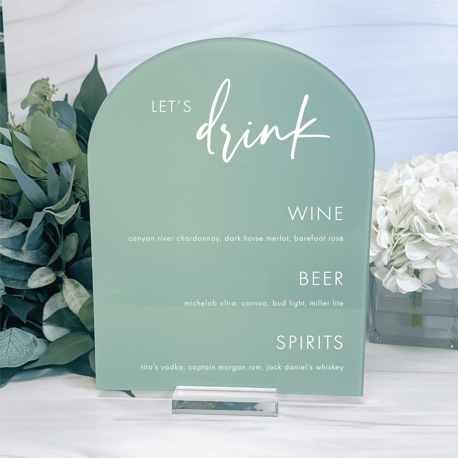 Sage green arched bar menu sign with white "Let's Drink" text and drink options for wine, beer, and spirits with descriptions.