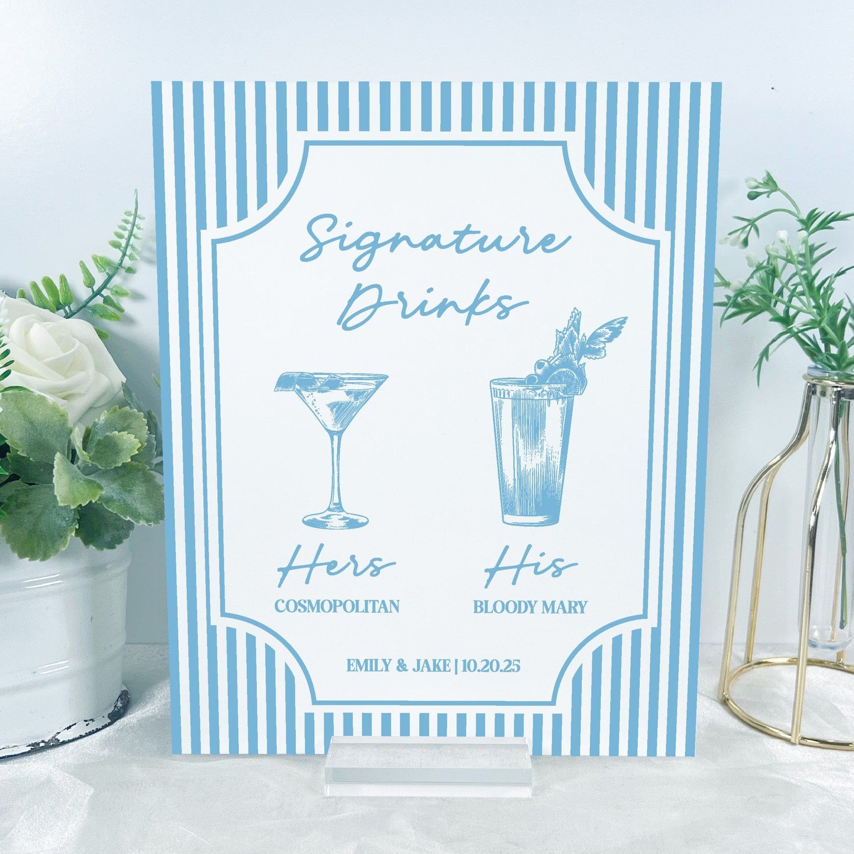 A rectangular acrylic wedding signature drinks sign features light blue and white stripes framing illustrations of two cocktails, designed to inform guests at an event bar.
