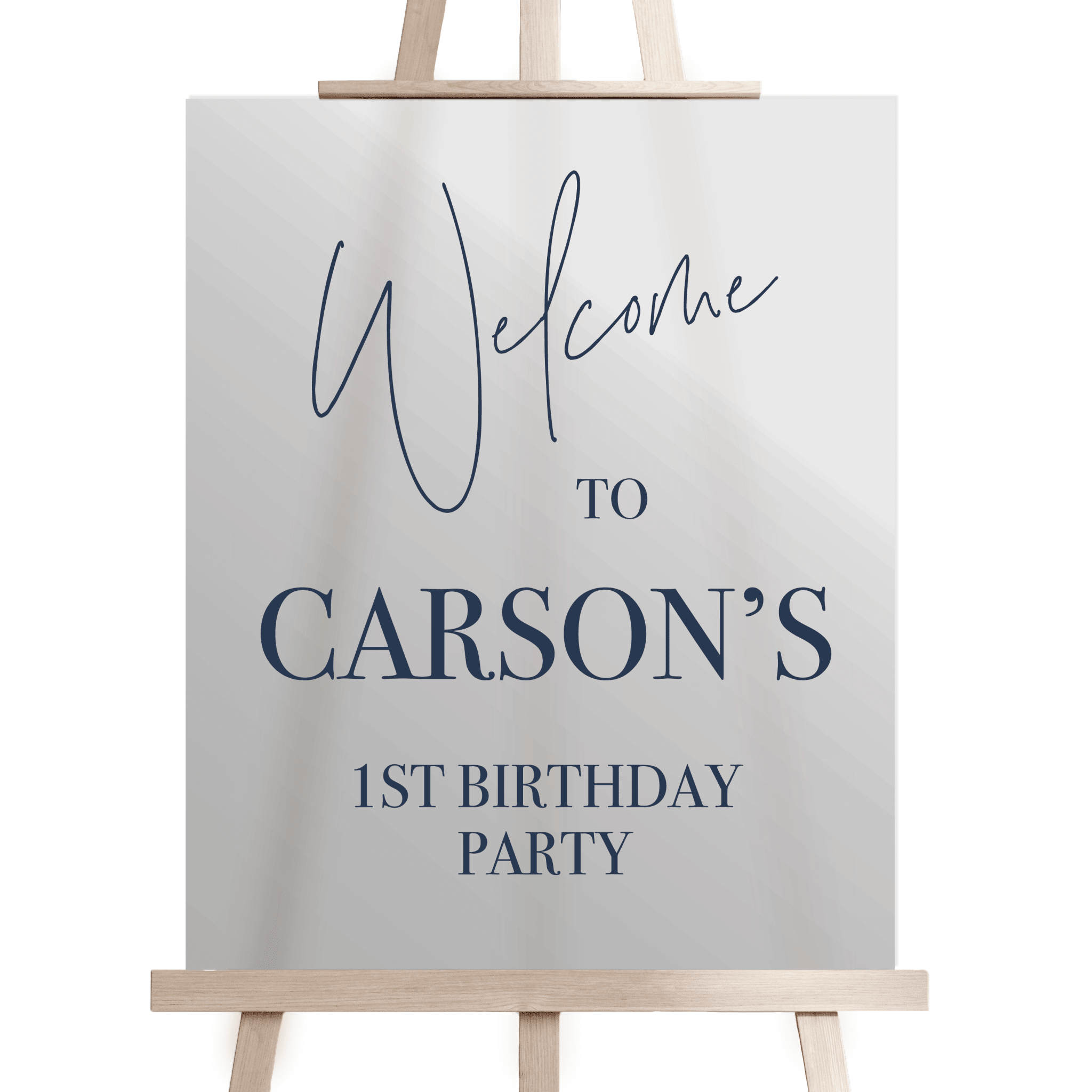 White welcome sign on wooden easel with "Welcome to Carson's 1st Birthday Party" in navy blue text