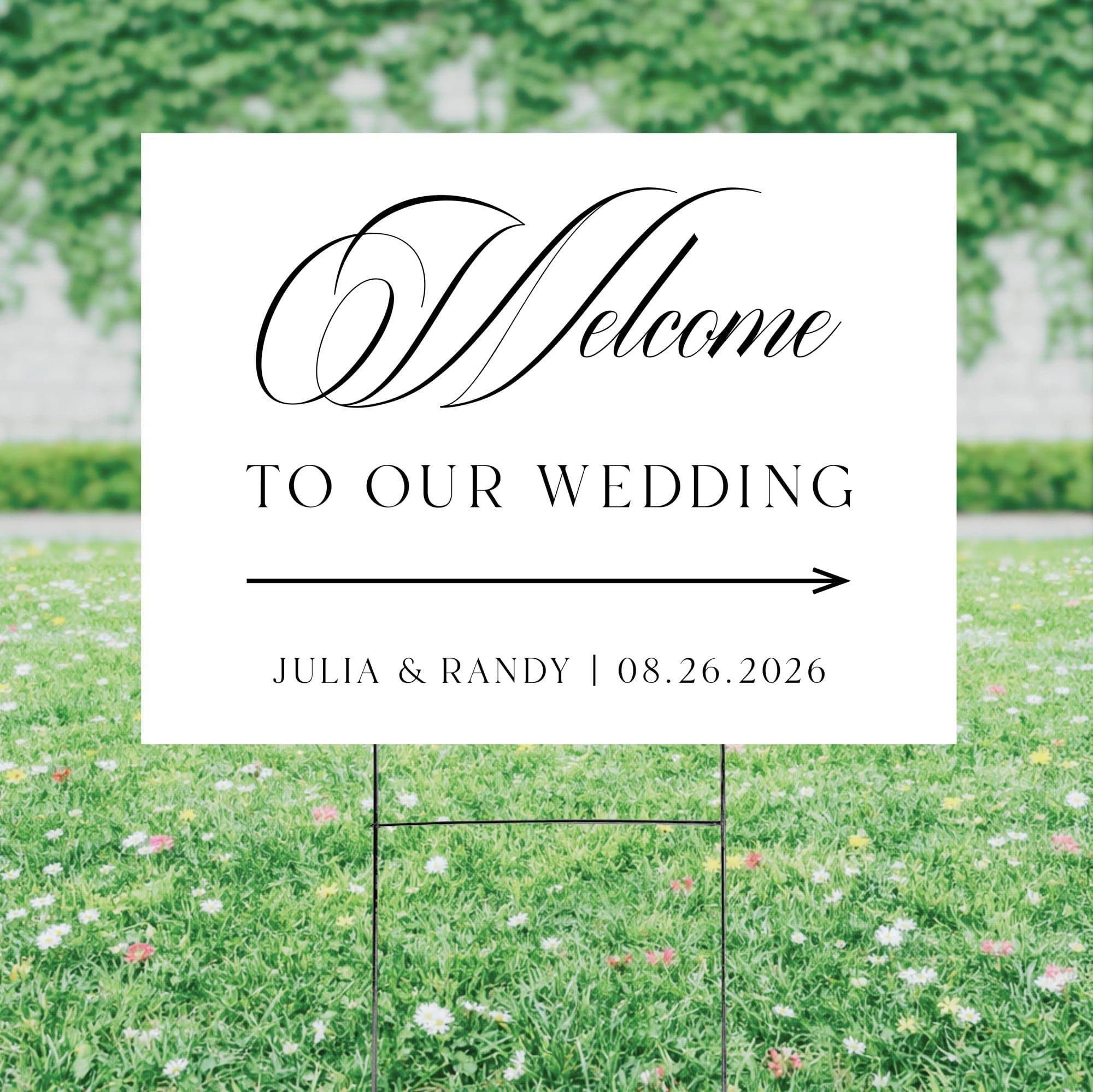 A white rectangular wedding welcome sign with elegant black script and an arrow graphic, made from a durable material and supported by a black metal H-stake, is displayed in a lush green lawn to direct guests.
