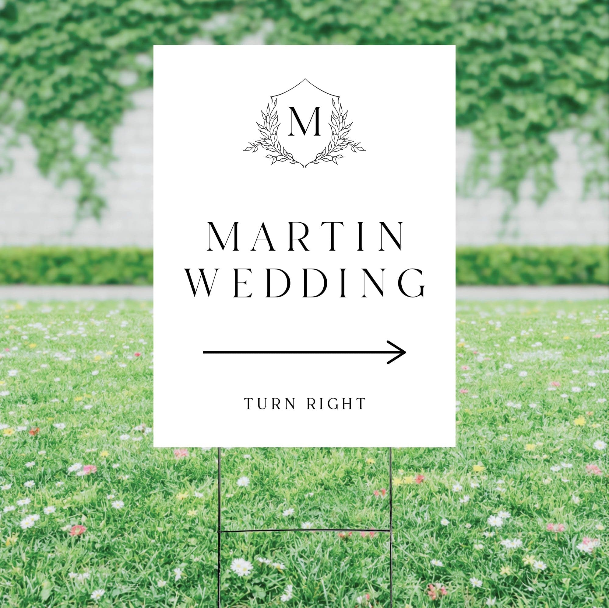 A personalized white wedding directional yard sign with a black monogram and arrow graphic, supported by a metal H-stake to guide guests.